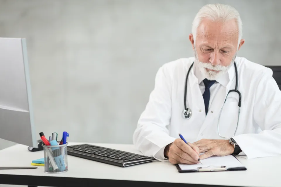 A doctor working at a desk with a computer and paperwork