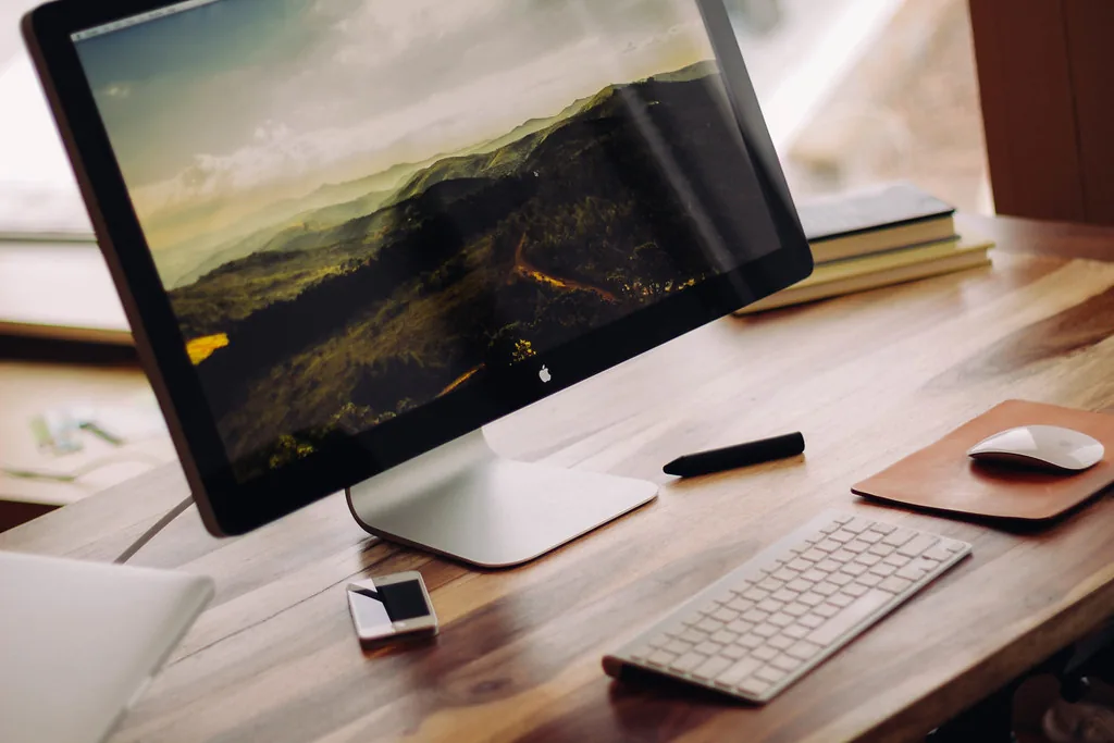 An all-in-one desktop computer, keyboard and mouse on a wooden desk
